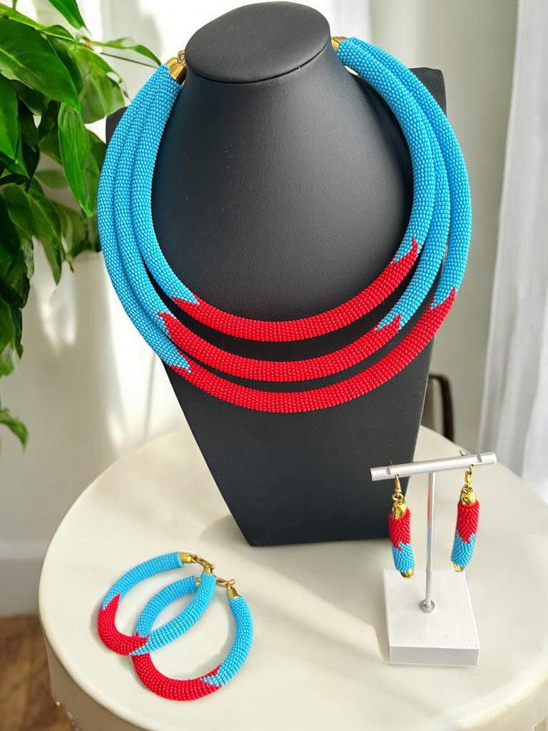 A necklace with a combination of blue and red beads, displayed on a mannequin bust. The necklace is paired with a matching set of earrings and bracelets, set on a white surface.